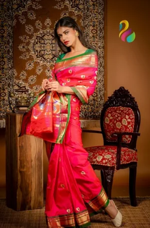 Woman wearing a vibrant pink saree with gold accents and intricate designs, standing beside a decorative chair.