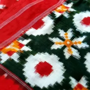 Close folded view of a Double Ikat pure cotton saree featuring traditional geometric motifs in green, red, white and orange, paired with a solid red body and fine striped red woven border.