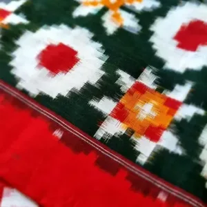 Close view of a Double Ikat pure cotton saree featuring traditional multicolor geometric motifs in green, white, red and orange, along with a solid red body and fine woven border detailing.