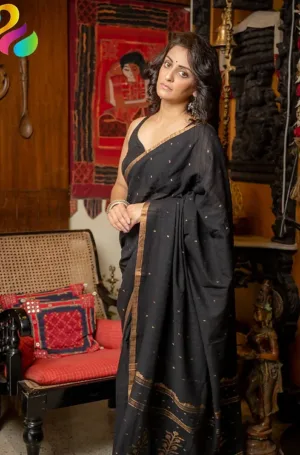 A woman wearing a black saree with gold accents, standing elegantly in a traditional setting with decorative elements.