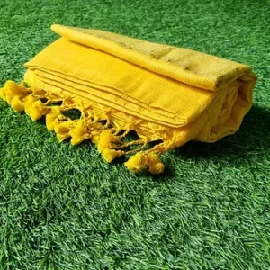 Folded yellow handloom Bengal cotton saree with tassel pallu, placed on green grass; lightweight traditional Bengal cotton saree design.