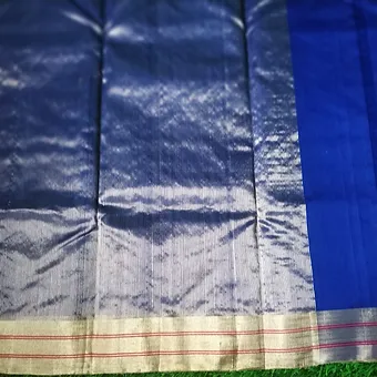 Royal Blue Chanderi Saree with Silver Zari Pallu & Pink Border Highlights Close view of a royal blue Chanderi silk–cotton saree featuring a shiny silver zari pallu with thin pink lines on the border, displayed on a grassy background.