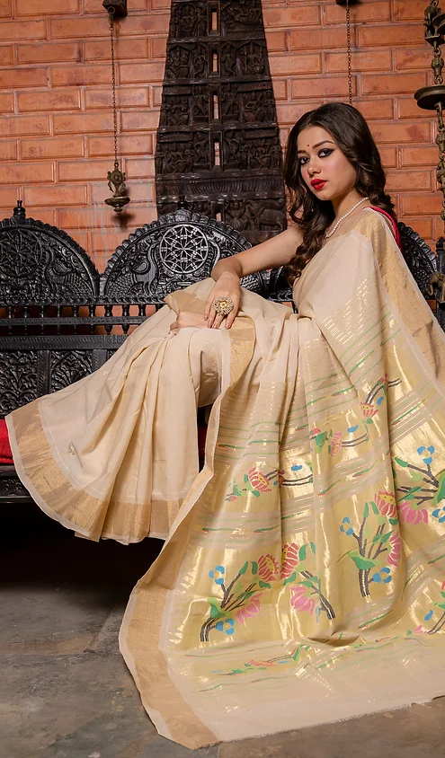 Handloom-Cotton-Paithani-1 A woman draped in a handloom cotton Paithani saree with intricate floral patterns, seated elegantly on a traditional bench.
