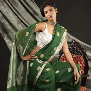 Woman wearing a green handloom cotton silk Chanderi saree with golden butti motifs and silver pallu, seated in a studio setup; elegant festive and party wear saree.