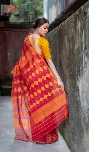 Red and mustard handloom Dhakai Jamdani saree with traditional geometric floral motifs, worn by woman in classic ethnic style