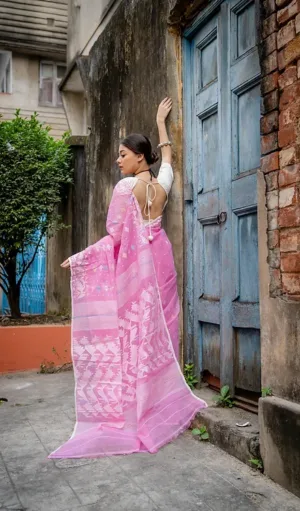 Back view of a model wearing a Handloom Dhakai Jamdani saree in soft pink, featuring intricate white floral and geometric motifs. The saree is draped with a sheer pallu and tie-back blouse