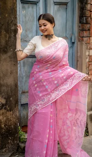Model wearing a Handloom Dhakai Jamdani saree in soft pink, featuring intricate white floral and geometric motifs along the border. The saree is elegantly draped with delicate patterns and a sheer pallu, offering a blend of traditional and modern charm."