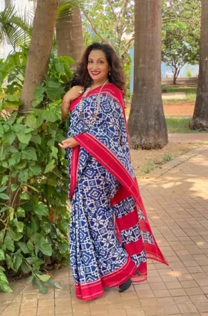 Woman wearing blue handloom double ikat cotton saree with white geometric patterns and red border