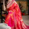Elegant woman draped in a Handloom Katan Silk Sona Roopa Banarasi saree with intricate gold zari work, featuring a vibrant pink color with floral and heart motifs. The saree is finished with a golden border, exuding traditional luxury and grace.