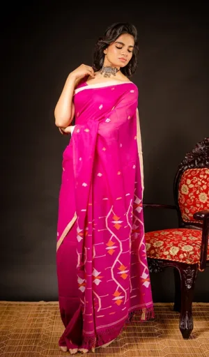 A woman draped in a pink Jamdani saree with intricate patterns, standing gracefully against a dark background.