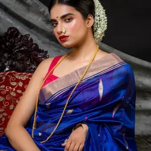 Woman wearing a royal blue pure silk Chanderi handloom saree with silver zari border and motifs, posing against a draped backdrop; elegant festive silk saree look.
