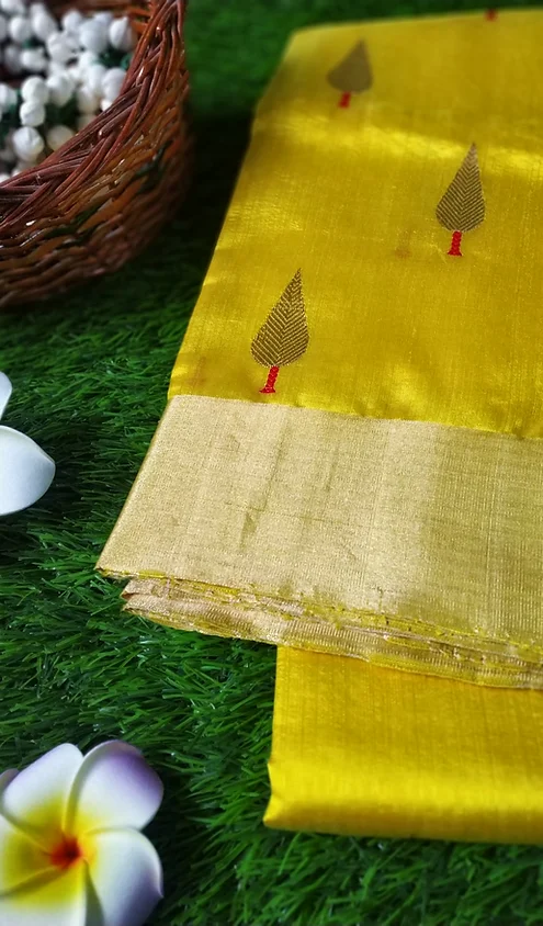 Handloom-Pure-Silk-Chanderi-Saree-3 Yellow handloom Chanderi saree with intricate tree motifs and a golden border, folded neatly on a textured surface.