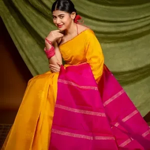Woman wearing a yellow and pink pure silk Kanjivaram handloom saree with delicate zari detailing, posing gracefully in a traditional indoor setup; classic festive silk saree look.