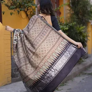 Back view of a handloom Tussar silk Mangalgiri saree featuring Ajrakh-style floral and geometric motifs in earthy beige, maroon and black shades, paired with a glossy black textured zari border, draped by a woman wearing a black blouse.