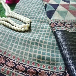 Close view of a handloom Tussar silk Mangalgiri saree featuring Ajrakh-style geometric and check patterns in muted teal, beige and maroon tones, paired with a textured black zari border and displayed with pearl jewelry