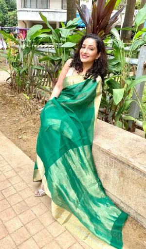 Woman wearing a green and gold handloom cotton silk Chanderi saree, seated outdoors with plants in the background.