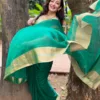 Woman wearing a green saree with a gold border, playfully posing outdoors near trees.