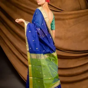 Woman wearing a blue and green handloom cotton silk Maheshwari saree with gold zari border and butti motifs, shown from the back in a studio setup; elegant festive saree look.