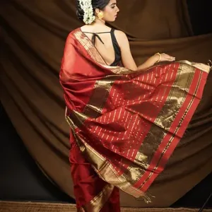 Woman wearing a maroon handloom cotton silk Maheshwari saree with rich gold zari pallu and striped detailing, posing in a traditional setup; elegant festive saree look.