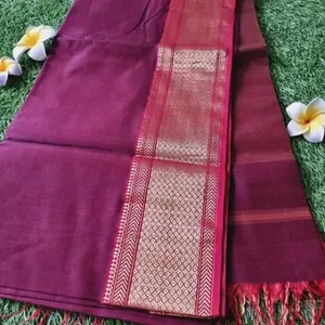Maroon handloom cotton silk Maheshwari saree with gold zari border and red tassels, displayed on green grass with flowers; elegant traditional Maheshwari saree.