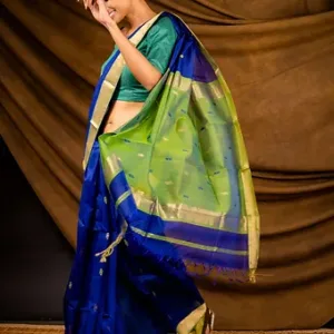 Woman wearing a blue and green handloom cotton silk Maheshwari saree with gold zari border and butti motifs, showing the pallu in a studio setting; elegant festive saree look.