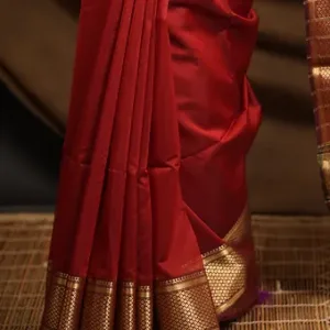 Woman wearing a maroon handloom cotton silk Maheshwari saree with rich gold zari border, standing on a woven mat; elegant traditional festive saree look.
