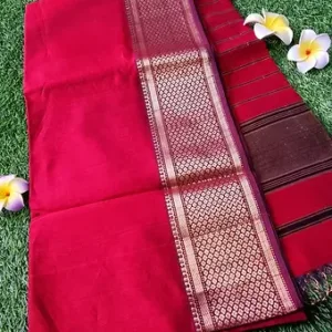 Red handloom cotton silk Maheshwari saree with rich gold zari border and striped pallu, displayed on green grass with flowers; elegant traditional Maheshwari saree.