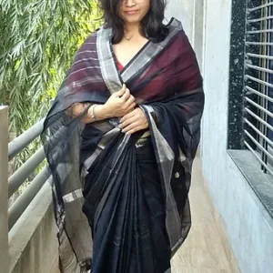 Woman wearing a black saree with a silver zari border, styled elegantly with a matching shawl, standing on a balcony.