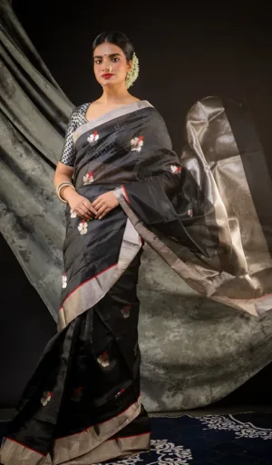 A woman draped in a black silk Chanderi saree with floral embroidery and a contrasting border, styled with traditional accessories.