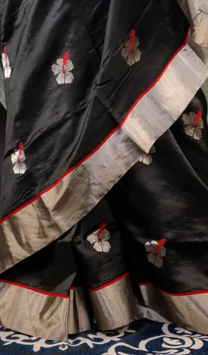 Black silk saree with intricate hibiscus flower embroidery and a contrasting silver border.