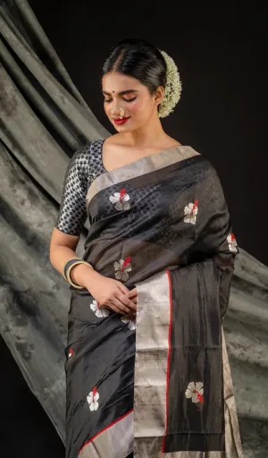 A woman wearing a black handloom silk Chanderi saree adorned with floral embroidery, paired with a patterned blouse and traditional accessories.