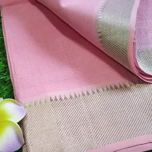 Close folded view of a pastel pink Mangalgiri handloom pure cotton saree featuring a fine textured weave and a detailed silver zari border with geometric patterning, displayed on a grass surface with floral decor.