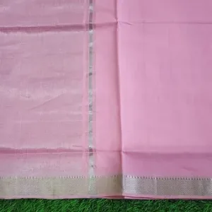 Close view of a pastel pink Mangalgiri handloom pure cotton saree featuring a plain woven body with a simple textured silver zari border, photographed against a green grass background