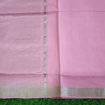 Pastel Pink Cotton Mangalgiri Saree with Simple Silver Zari Border Close view of a pastel pink Mangalgiri handloom pure cotton saree featuring a plain woven body with a simple textured silver zari border, photographed against a green grass background