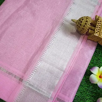 Light Pink Pure Cotton Mangalgiri Saree with Silver Border Close view of a light pink Mangalgiri handloom pure cotton saree featuring a simple textured weave and a broad silver zari border, displayed on a green grass background with decorative elements.
