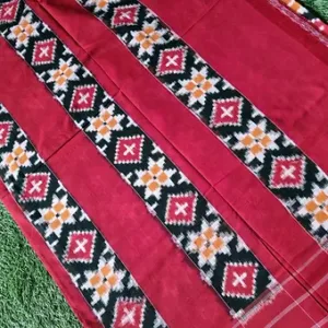 Red handloom pure cotton double ikat saree with black, white and yellow geometric ikat border design, displayed on green grass; vibrant traditional cotton saree.