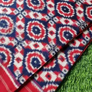 Red and navy blue handloom pure cotton double ikat saree with geometric circular ikat patterns, displayed on green grass; vibrant traditional cotton saree.