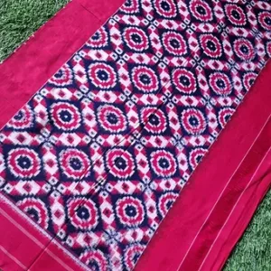 Red handloom pure cotton double ikat saree with multicolor geometric ikat pallu design, displayed on green grass; vibrant traditional cotton saree style.