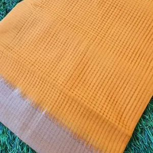 Mustard handloom pure cotton Mangalagiri saree with fine checked weave and subtle zari border, displayed flat on grass; lightweight traditional cotton saree.