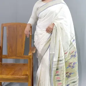 A woman wearing a handloom pure cotton Paithani saree with intricate designs, standing beside a wooden chair.