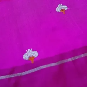 Close-up view of a vibrant pink handloom fabric with intricate white floral embroidery and a silver border.