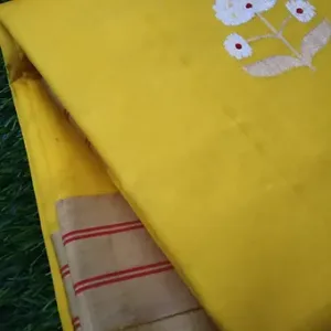 Folded yellow pure silk Chanderi saree featuring delicate white floral butta embroidery and a beige zari border with red striped detailing, placed on a grass background