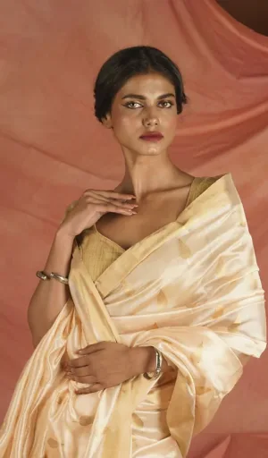 Model wearing a handloom pure silk Chanderi saree with a light peach color and gold motifs, styled elegantly with a simple blouse.