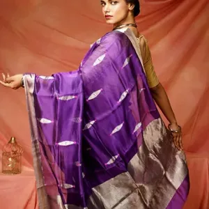 Woman wearing a purple pure silk Chanderi handloom saree with silver zari border and leaf motifs, posing against a soft peach backdrop; elegant festive silk saree look.