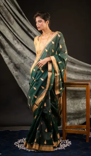 Chanderi saree in dark green with golden motifs and borders, worn by a model standing beside a wooden stool.