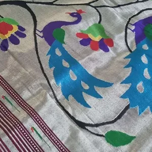 Handloom pure silk fabric with intricate peacock and floral motifs in vibrant colors on a silver background.