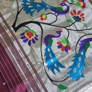 Handloom pure silk fabric featuring intricate peacock and floral designs in vibrant colors on a silver background.