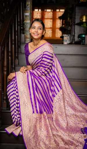 Woman wearing a purple and beige handwoven saree with intricate patterns, seated on a staircase with a smile.