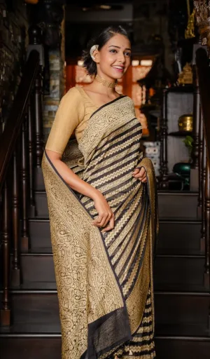 Woman wearing a handwoven pure khaddi georgette Banarasi saree with intricate gold patterns and a black border, standing on a staircase.