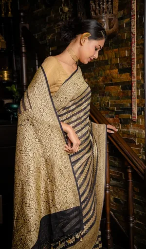 Woman wearing a handwoven pure khaddi georgette Banarasi saree with intricate gold patterns and a black border, descending a staircase.